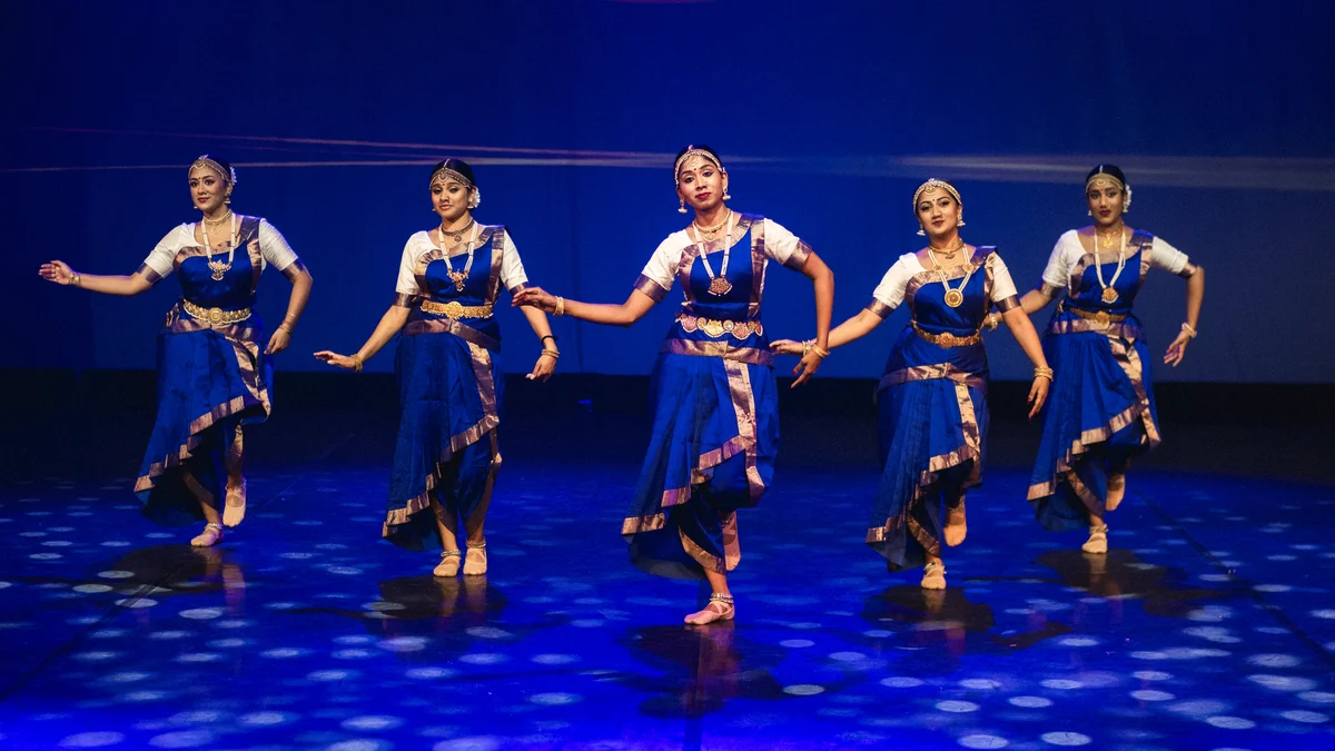 Five dancers performing in matching blue costumes with ivory sleeves and gold borders.